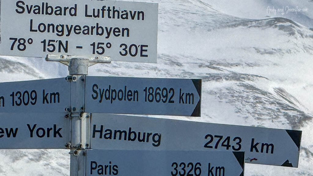 Svalbard distance signpost with snowy mountain backdrop.