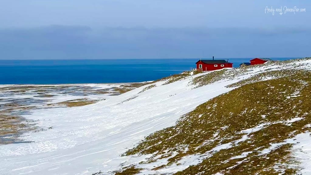 Red cabins on snowy slope by Arctic Ocean