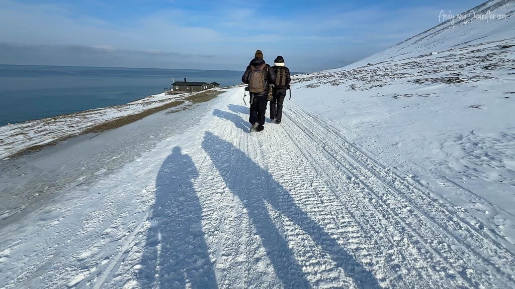 People walking snowy coastal trail in Svalbard