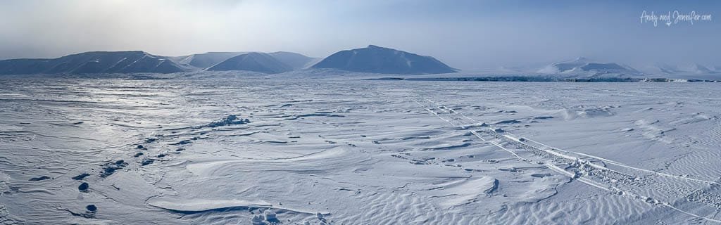 Vast Arctic tundra with snowmobile tracks and mountains