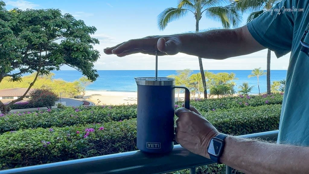 Person pressing French press coffee with ocean view