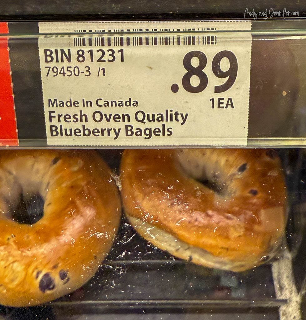 Display of fresh oven-baked blueberry bagels priced at 89 cents each, labeled “Made in Canada” inside a bakery or grocery store.