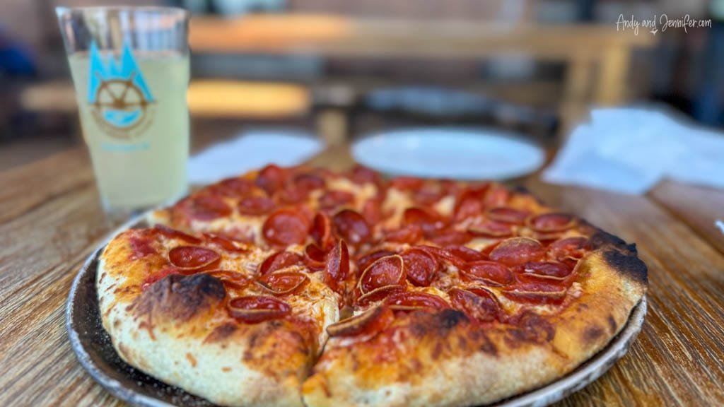 Close-up of a pepperoni pizza with crispy crust served on a wooden table alongside a cold drink in a glass.