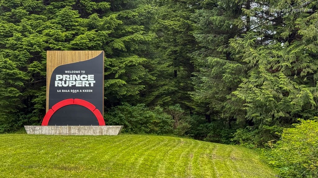 Welcome sign for Prince Rupert, British Columbia, surrounded by dense green forest, featuring both English and an Indigenous language.