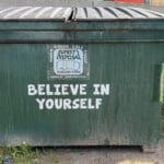 Green dumpster with bold "Believe in Yourself" message
