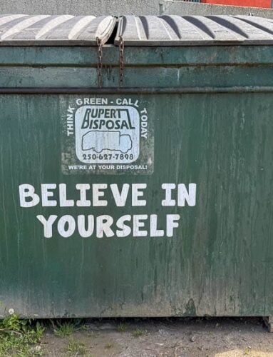 Green dumpster with bold "Believe in Yourself" message