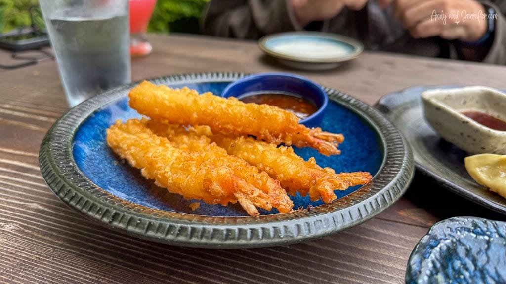 Plate of crispy golden tempura shrimp served with dipping sauce on a blue ceramic dish.