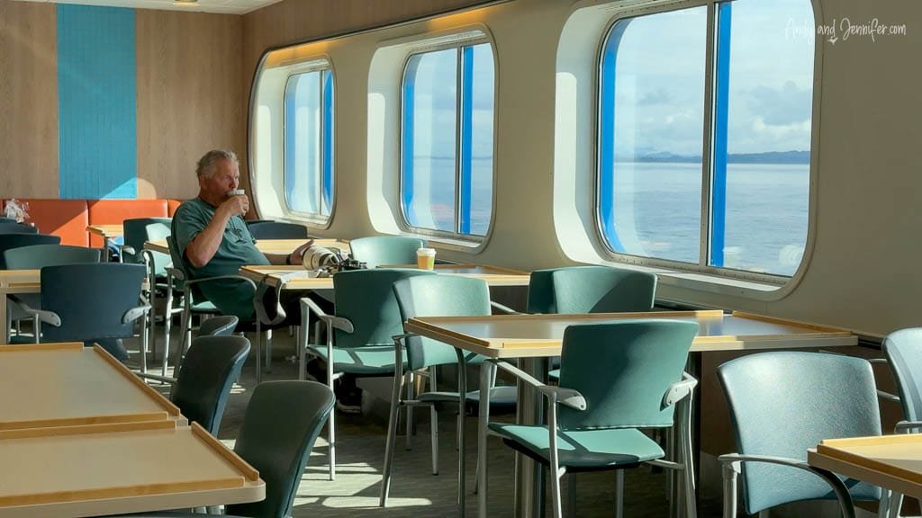 Man drinking coffee in ferry dining area with ocean view.