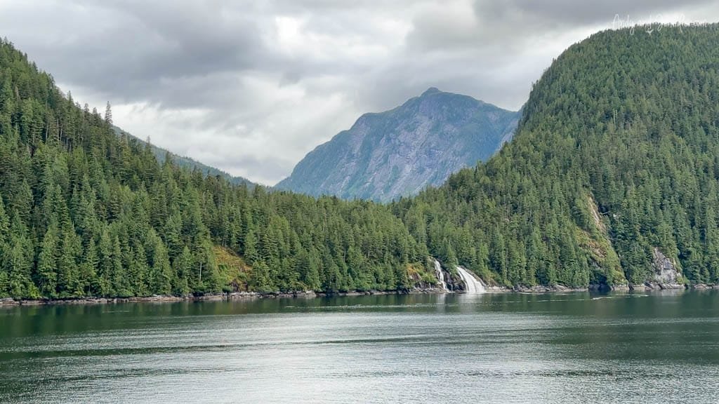 Scenic view of forested mountains and a waterfall flowing into the ocean.