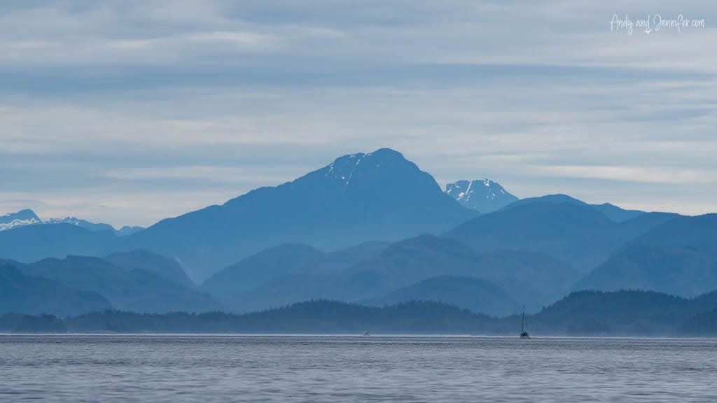 Blue mountain range with sailboat on calm ocean under cloudy sky