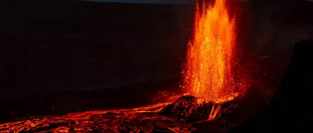 Lava fountain erupting at night with glowing flow