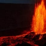 Lava fountain erupting at night with glowing flow