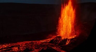 Lava fountain erupting at night with glowing flow