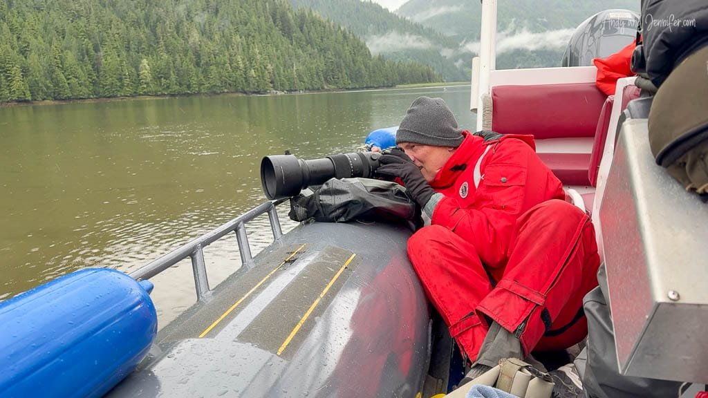 Photographer in red suit using telephoto lens on boat.