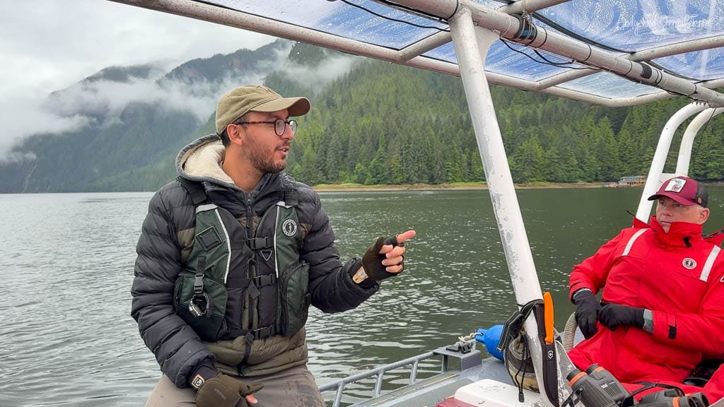 Tour guide explaining on boat in forested inlet.