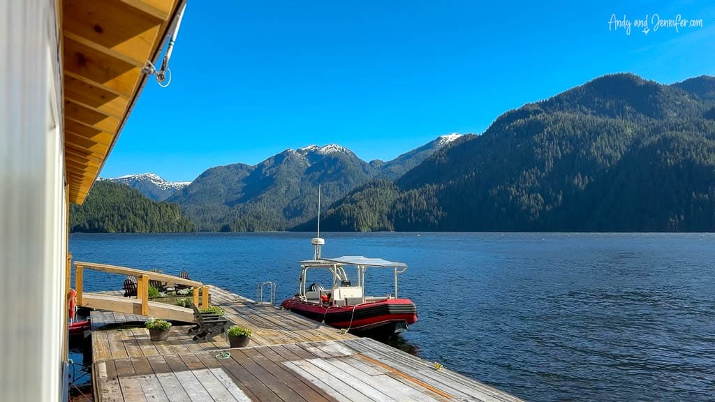 Sunny dock with red boat and forested mountain view.
