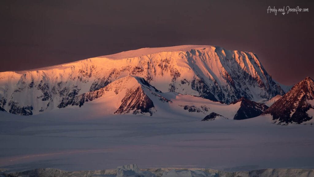 Antarctic mountain range lit by warm sunset light with snow and ice slopes