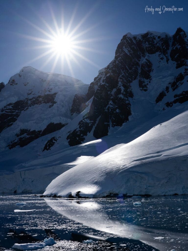 Bright Antarctic sunlight over snow-covered mountains and calm icy waters near Hidden Bay along the Antarctic Peninsula