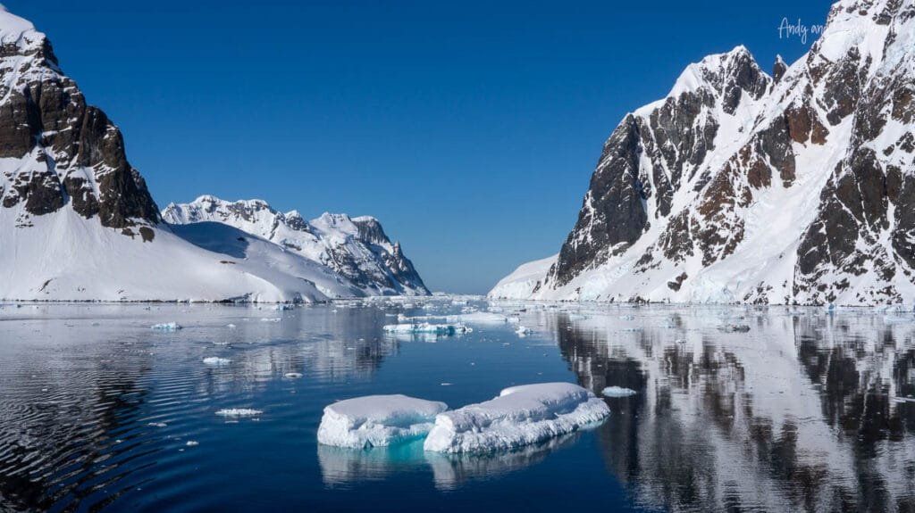 Sun reflecting across mirror-like Antarctic waters beneath snow-covered mountains near Hidden Bay in Antarctica