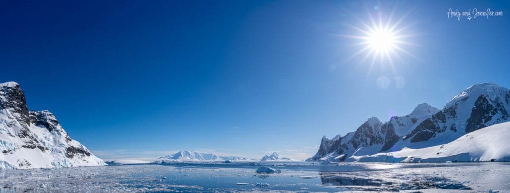 Panoramic view of calm Antarctic waters, floating sea ice, and snow-covered mountains near Hidden Bay along the Antarctic Peninsula