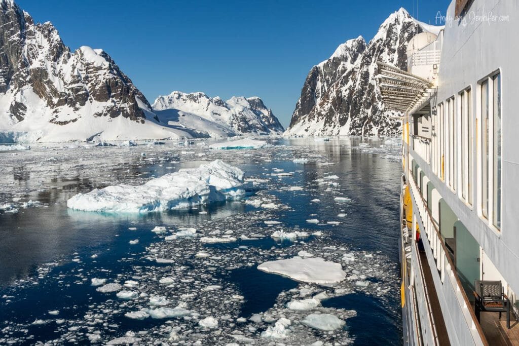 Expedition ship cruising through the Lemaire Channel in Antarctica surrounded by floating sea ice, glaciers, and dramatic snow-covered mountains
