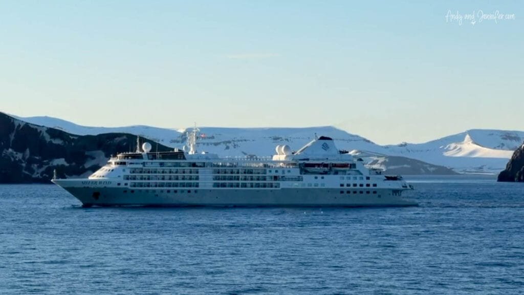 Small expedition cruise ship sailing through Antarctica with glaciers and ice cliffs in the distance