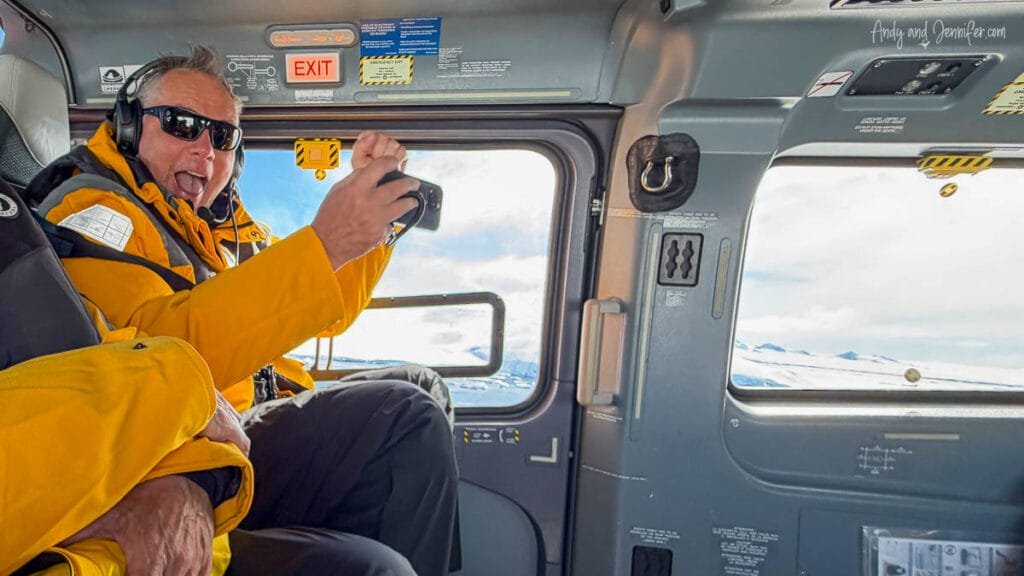 Traveler in expedition gear taking photos through helicopter window over Antarctic sea ice