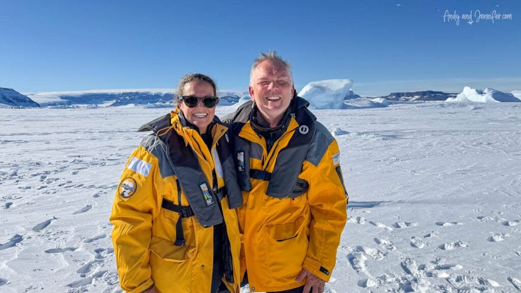 Travelers wearing Quark expedition parkas standing on sea ice in Antarctica with icebergs in background