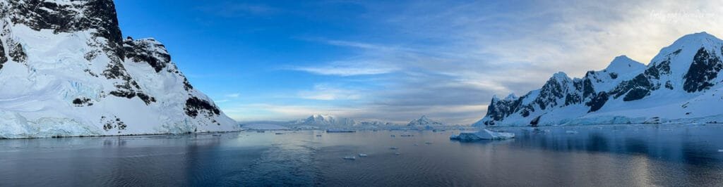 Panoramic view of calm waters, floating sea ice, and snow-covered mountains near the Lemaire Channel in Antarctica