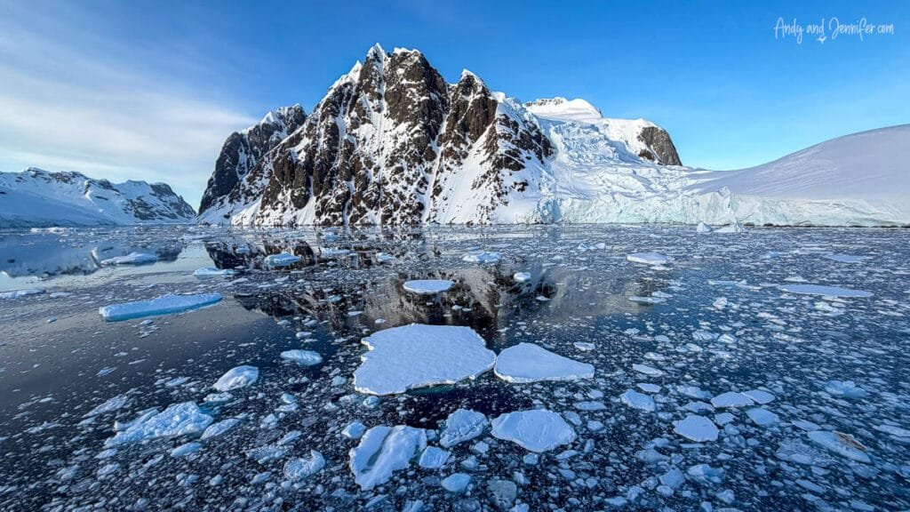 Snow-covered Antarctic mountains reflected in calm icy waters filled with floating sea ice near the Lemaire Channel in Antarctica