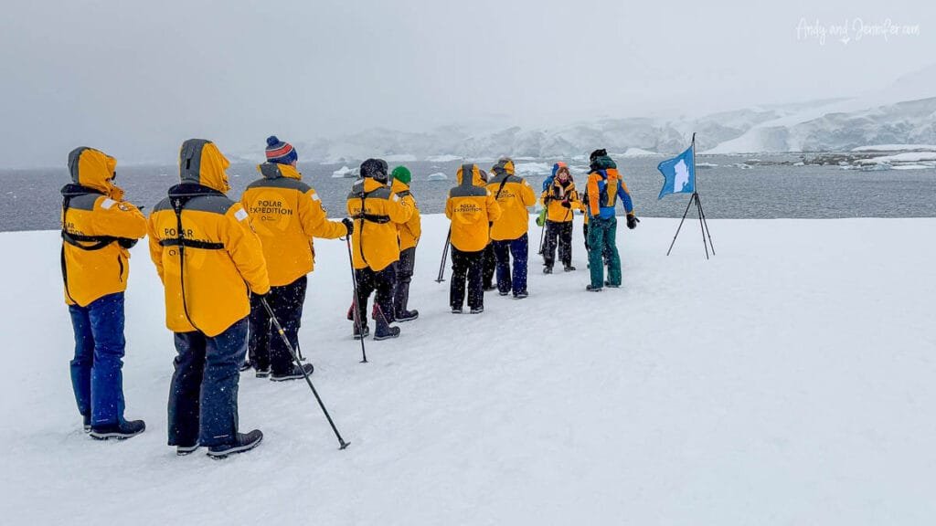 Passengers waiting in line for photos beside the Antarctic continent flag during a snowstorm at Portal Point on the Antarctic Peninsula.