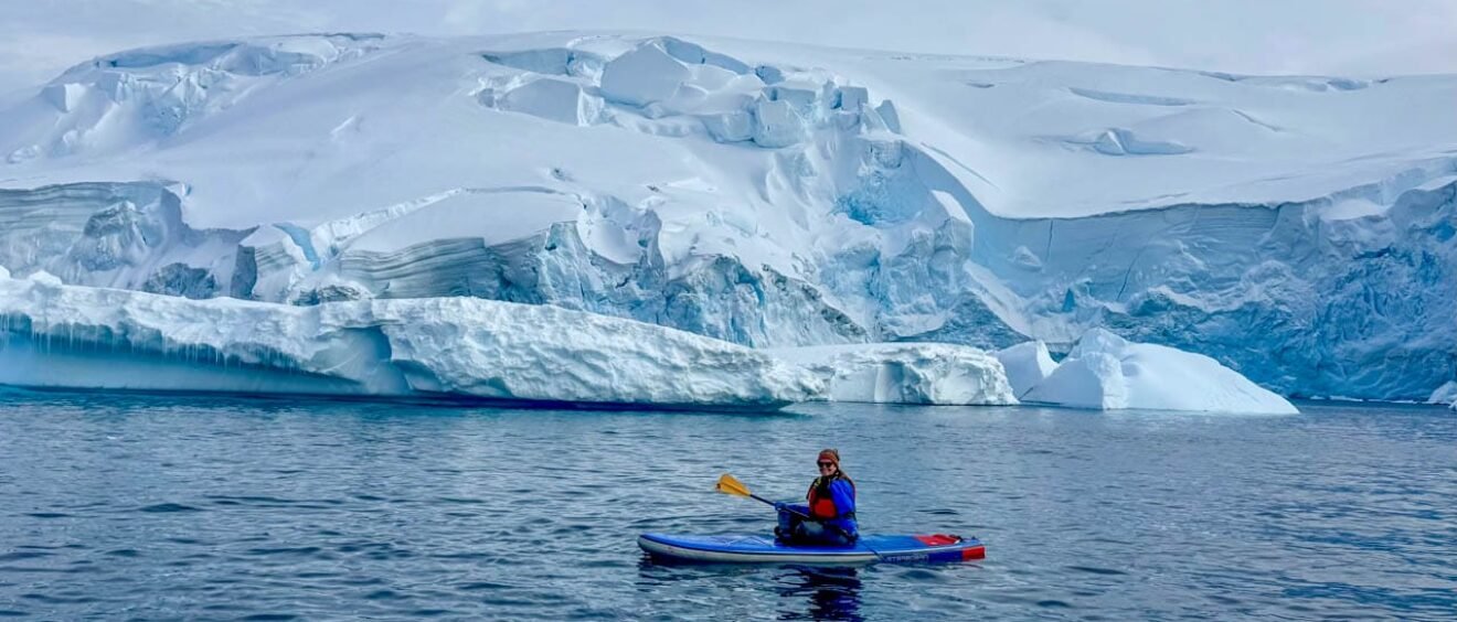 Woman stand up paddleboarding in Antarctica near Tower Island surrounded by icebergs and glaciers during an Antarctic Peninsula expedition cruise