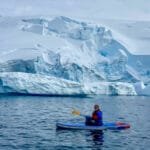 Woman stand up paddleboarding in Antarctica near Tower Island surrounded by icebergs and glaciers during an Antarctic Peninsula expedition cruise