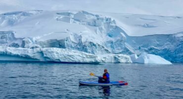 Woman stand up paddleboarding in Antarctica near Tower Island surrounded by icebergs and glaciers during an Antarctic Peninsula expedition cruise