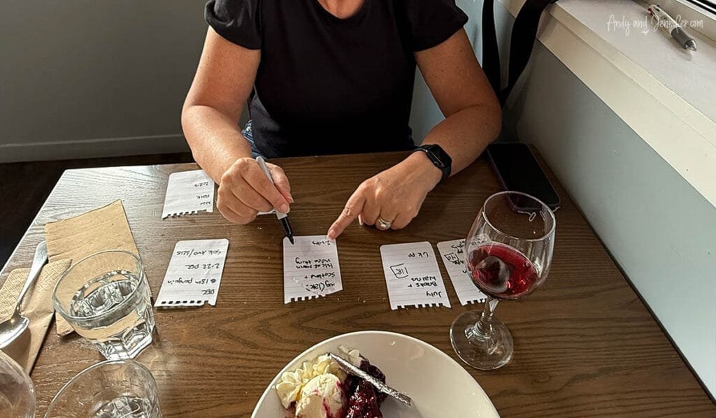 Person sitting at a cafe table, writing on small pieces of paper.