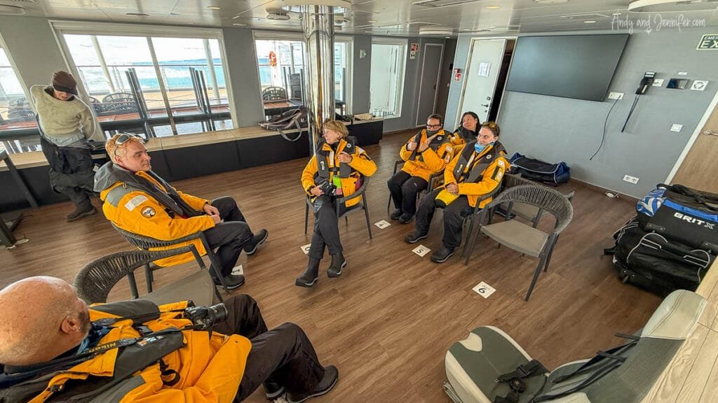 Passengers in expedition gear sitting in numbered chairs on and Antarctica expedition ship