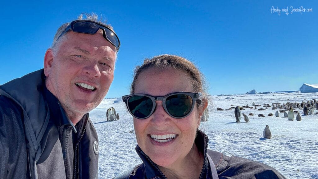 Couple smiling for selfie with emperor penguin colony in background in Antarctica