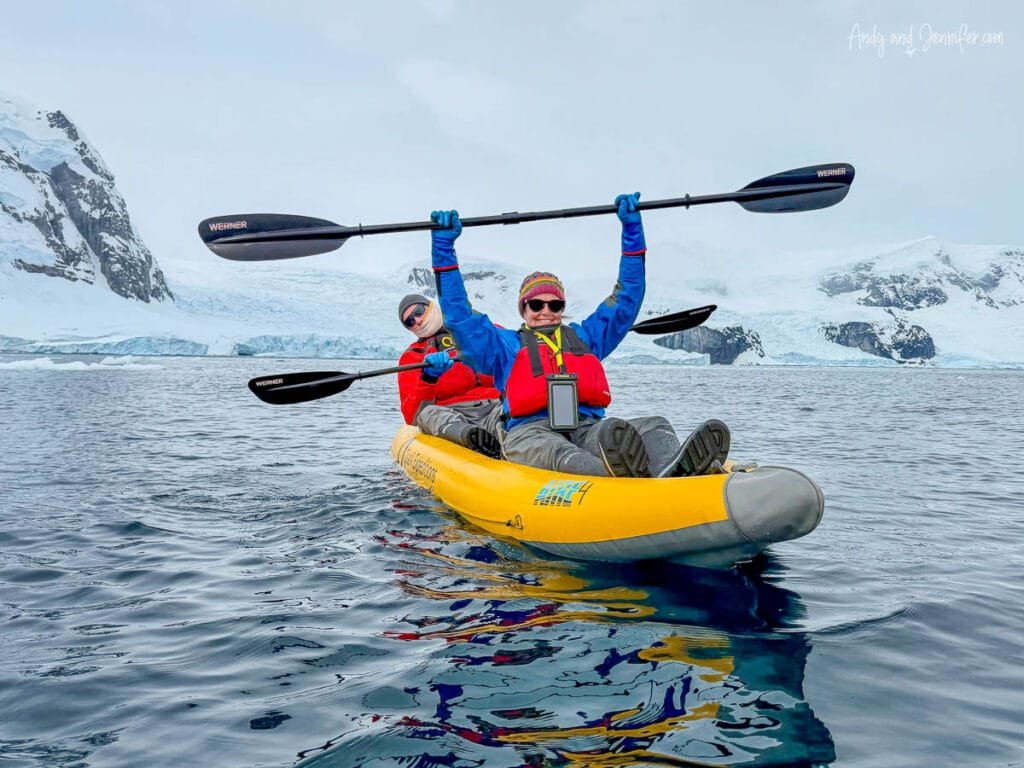 Two people paddling an inflatable kayak in Antarctica near Danco Island with snowy mountains, glaciers, and calm Antarctic waters in the background