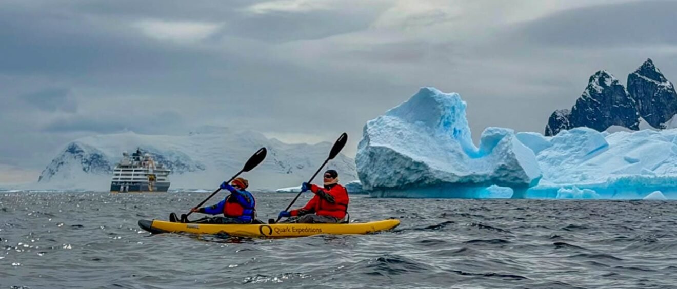 Two people kayaking in Antarctica near Danco Island surrounded by icebergs and Antarctic mountains during a paddling excursion along the Antarctic Peninsula