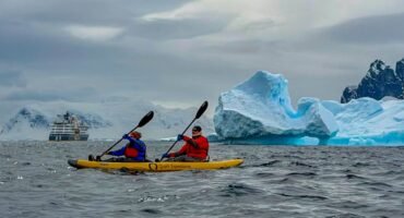 Two people kayaking in Antarctica near Danco Island surrounded by icebergs and Antarctic mountains during a paddling excursion along the Antarctic Peninsula