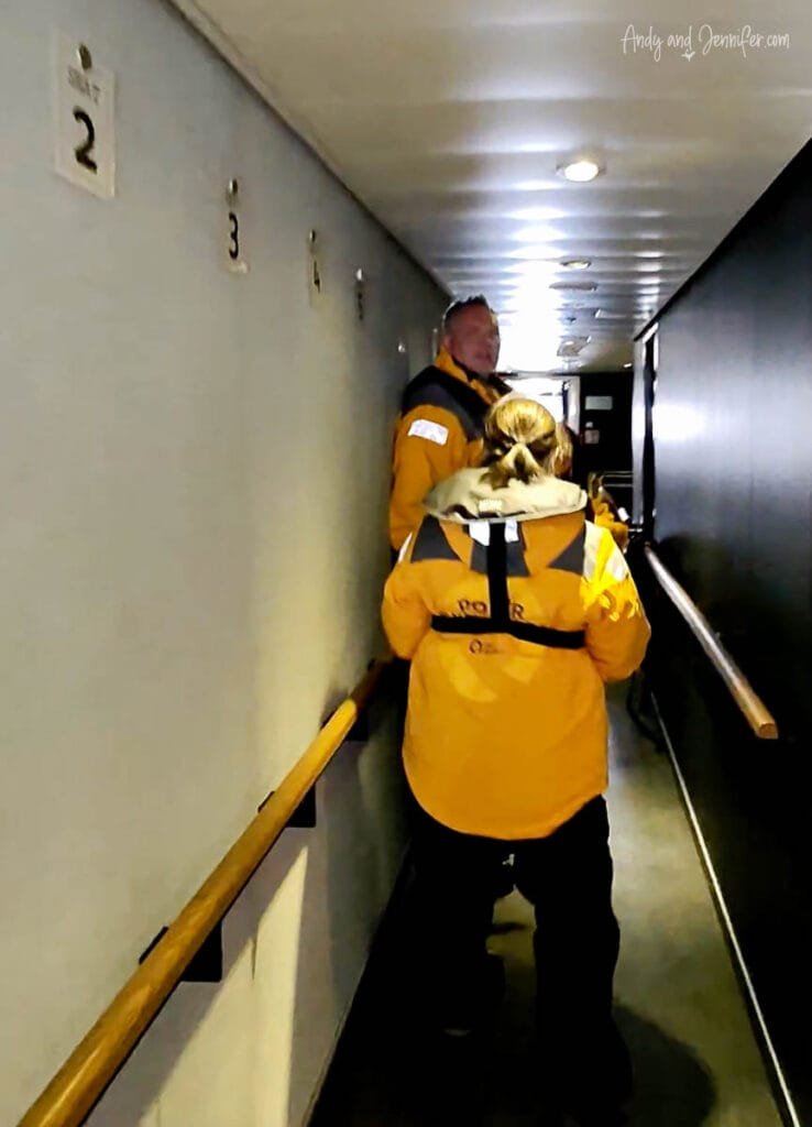 Travelers wearing life vests and parkas queueing in ship corridor before helicopter flight to Antarctic landing site