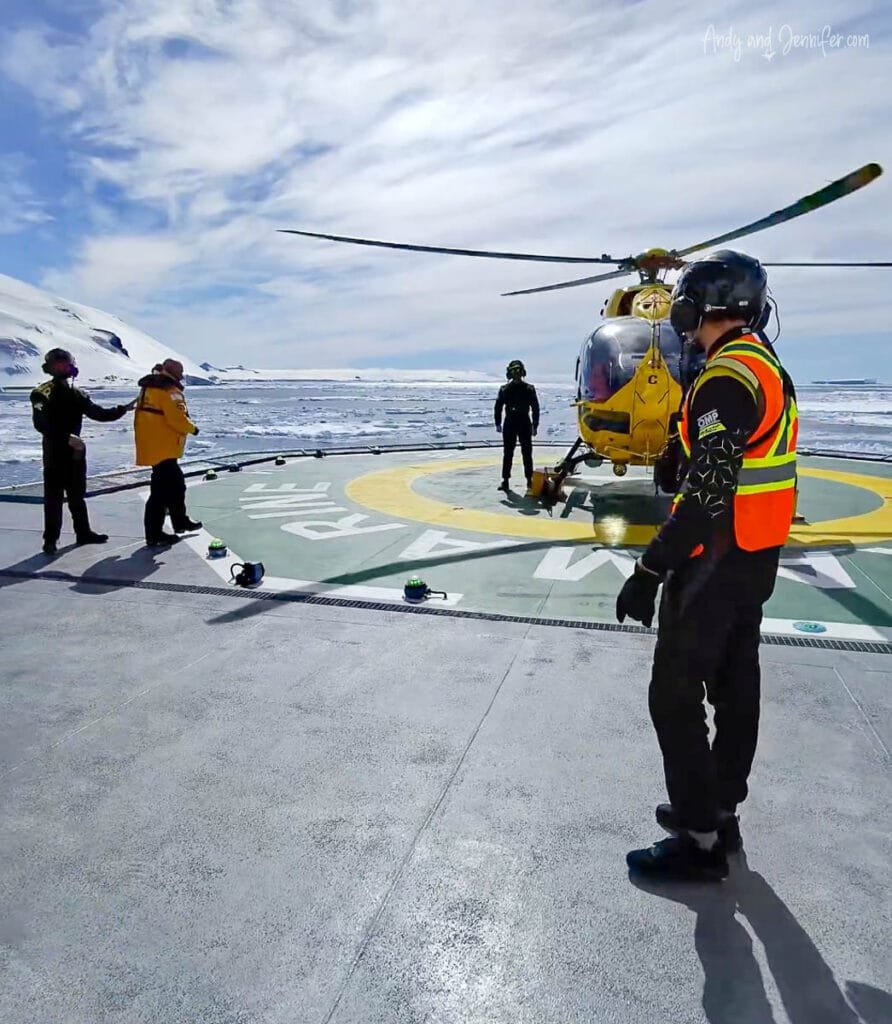 Helicopter on ship helipad with crew guiding passengers during Antarctic expedition flight operations