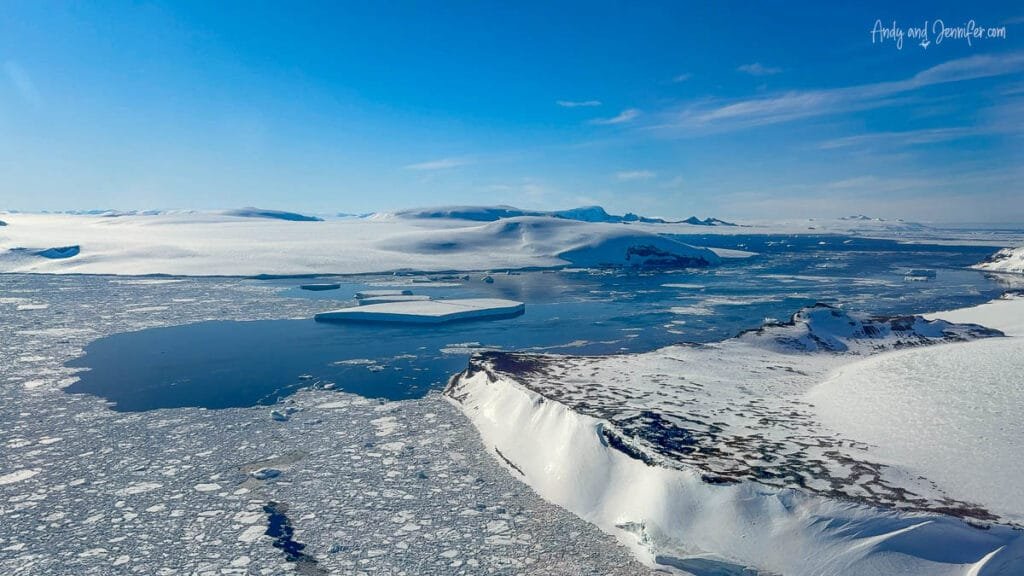 Wide aerial scene of sea ice, open water, and snowy coastline in Antarctica