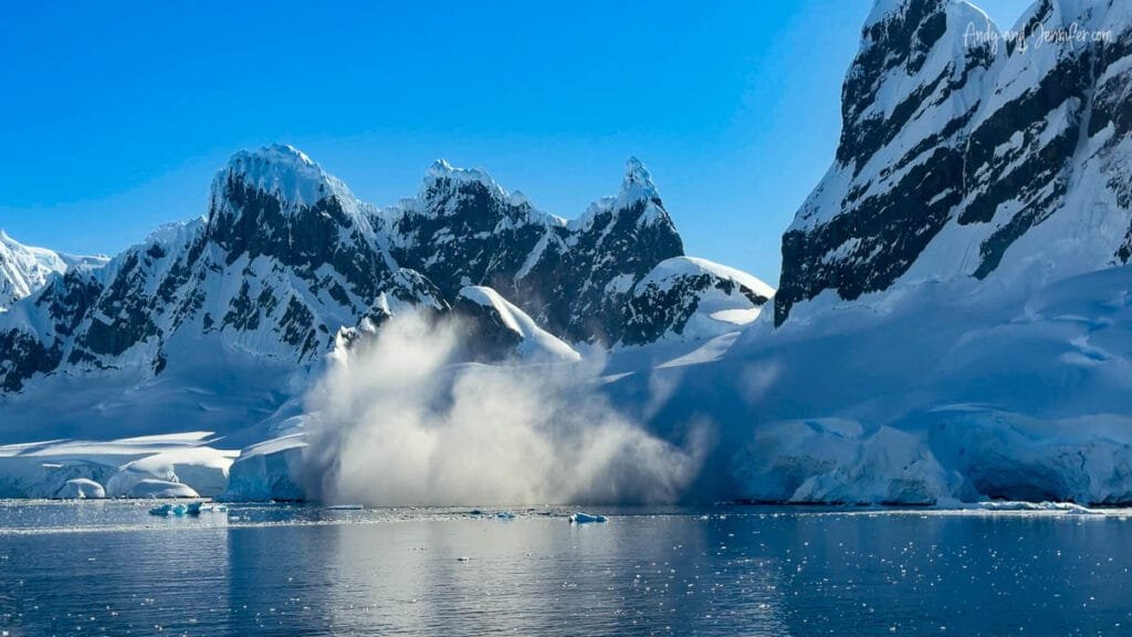 Avalanche crashing down snowy Antarctic mountains into the calm waters of the Antarctic Peninsula.