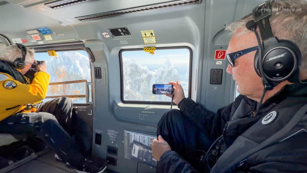 Passengers photographing Antarctic mountains from inside a helicopter during a flightseeing excursion over the Antarctic Peninsula.