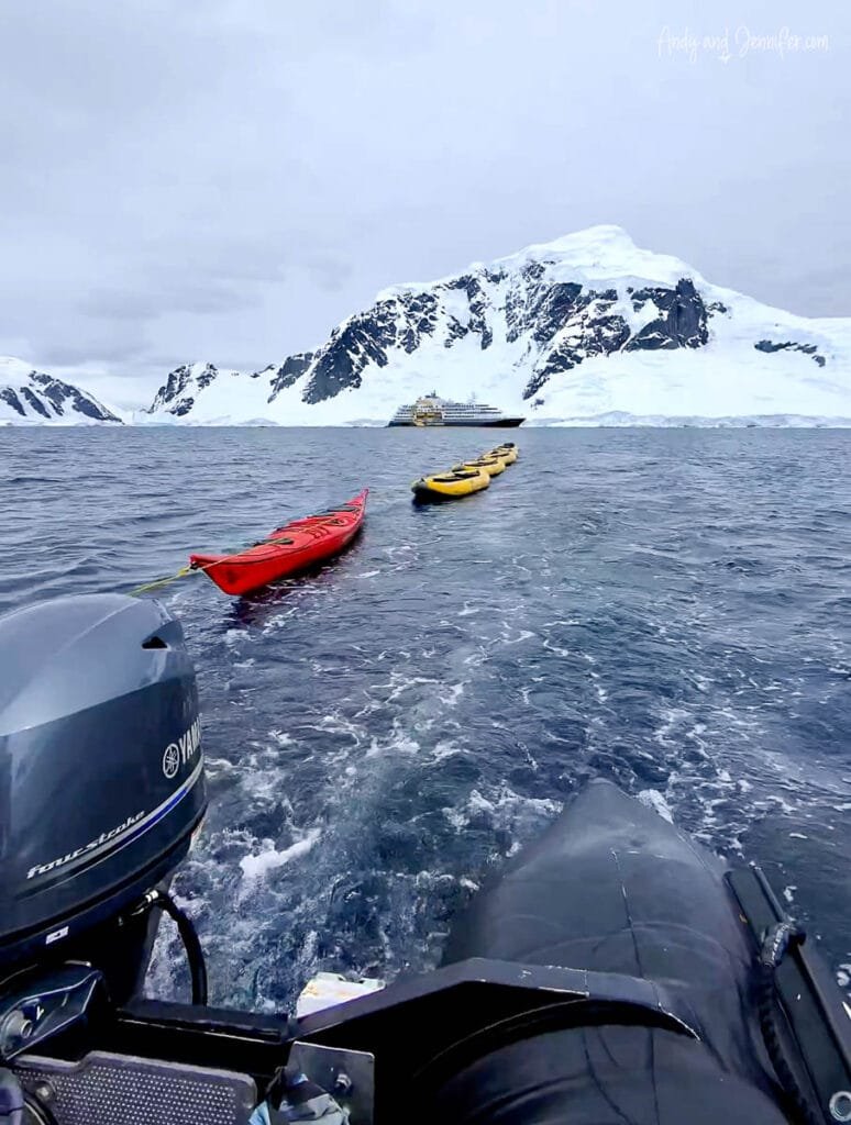 Inflatable kayaks being towed by Zodiac near Danco Island with Antarctic mountains and expedition ship along the Antarctic Peninsula