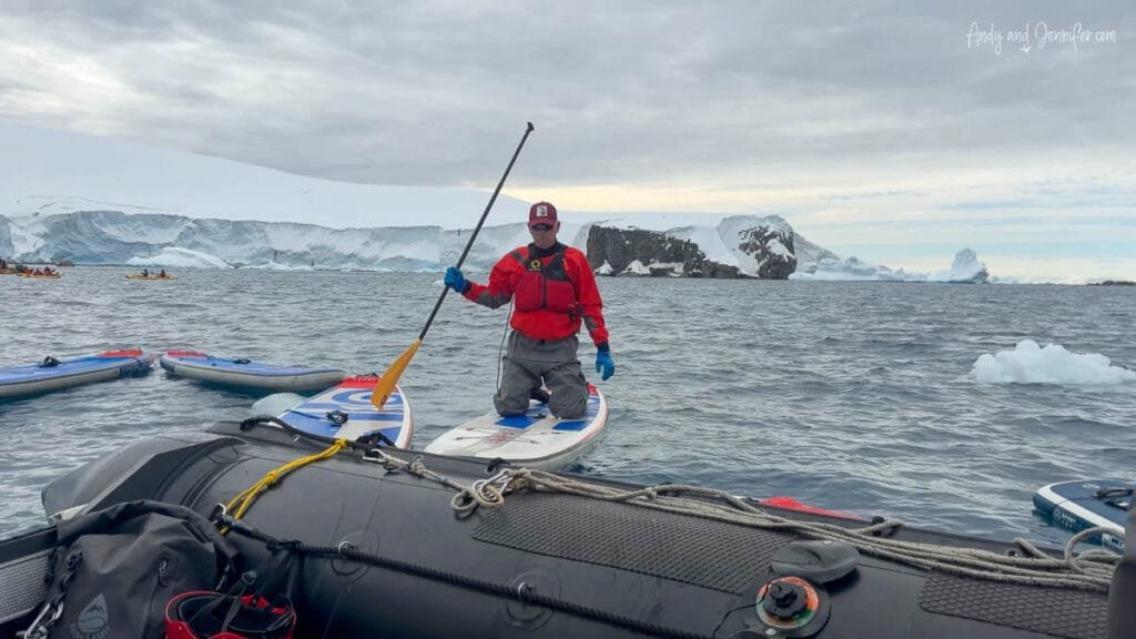 Passenger kneeling on an inflatable stand up paddleboard in Antarctica near Tower Island surrounded by glaciers, icebergs, and Antarctic scenery