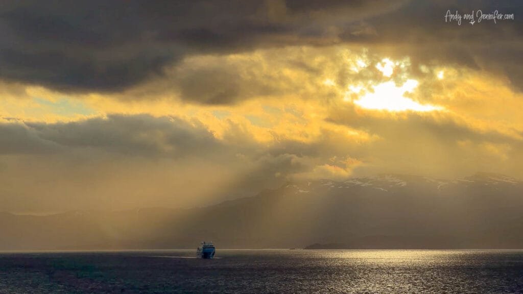 Expedition ship sailing near Ushuaia beneath dramatic storm clouds and golden sunrise light at the end of an Antarctica expedition cruise
