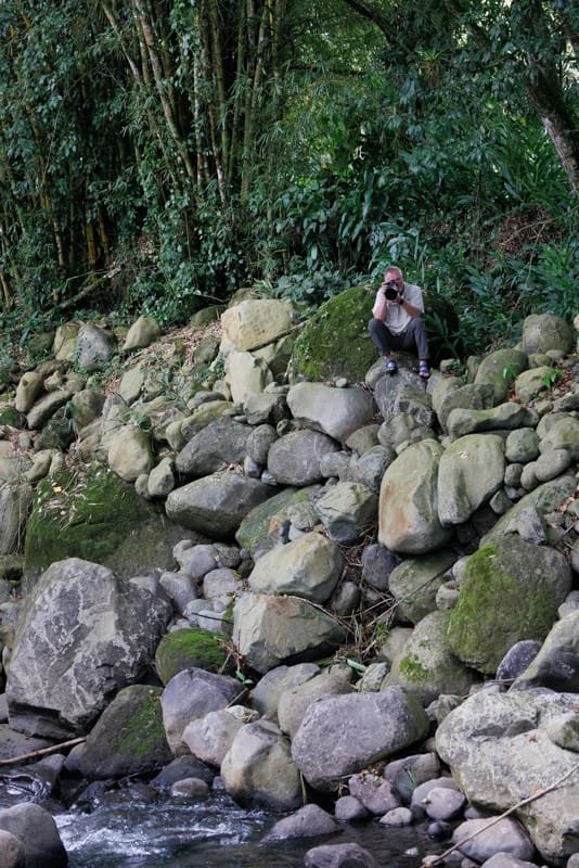 Photographer perched on a rocky riverbank while photographing a Sunbittern near Rancho Naturalista, Costa Rica.