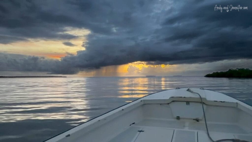 Small boat crossing calm water at sunrise near Bocas del Toro, Panama, with rain showers on the horizon.